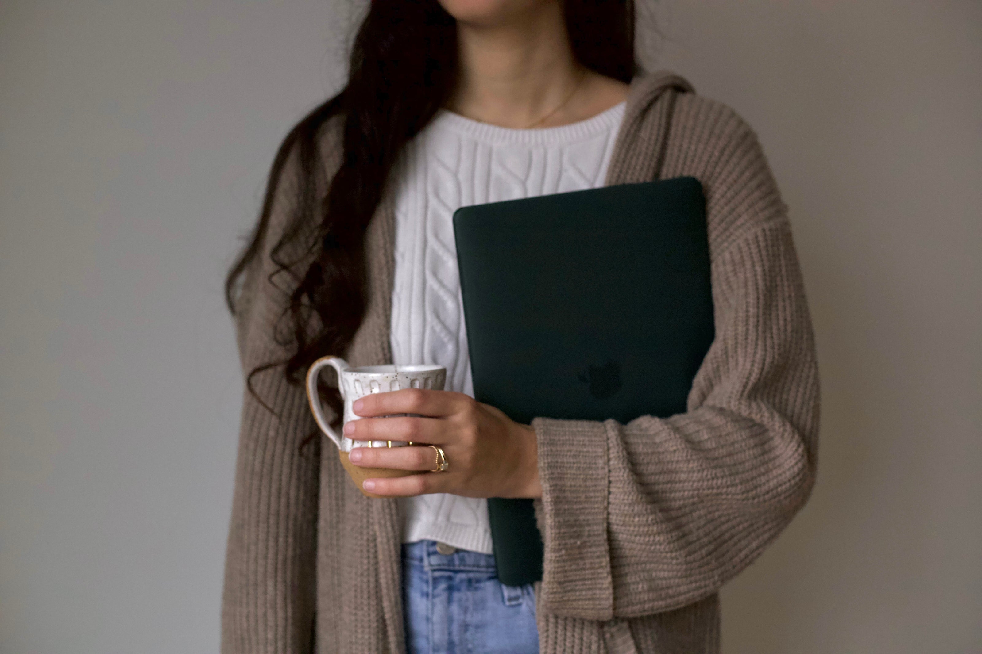Person holding a laptop and a mug with a plain background
