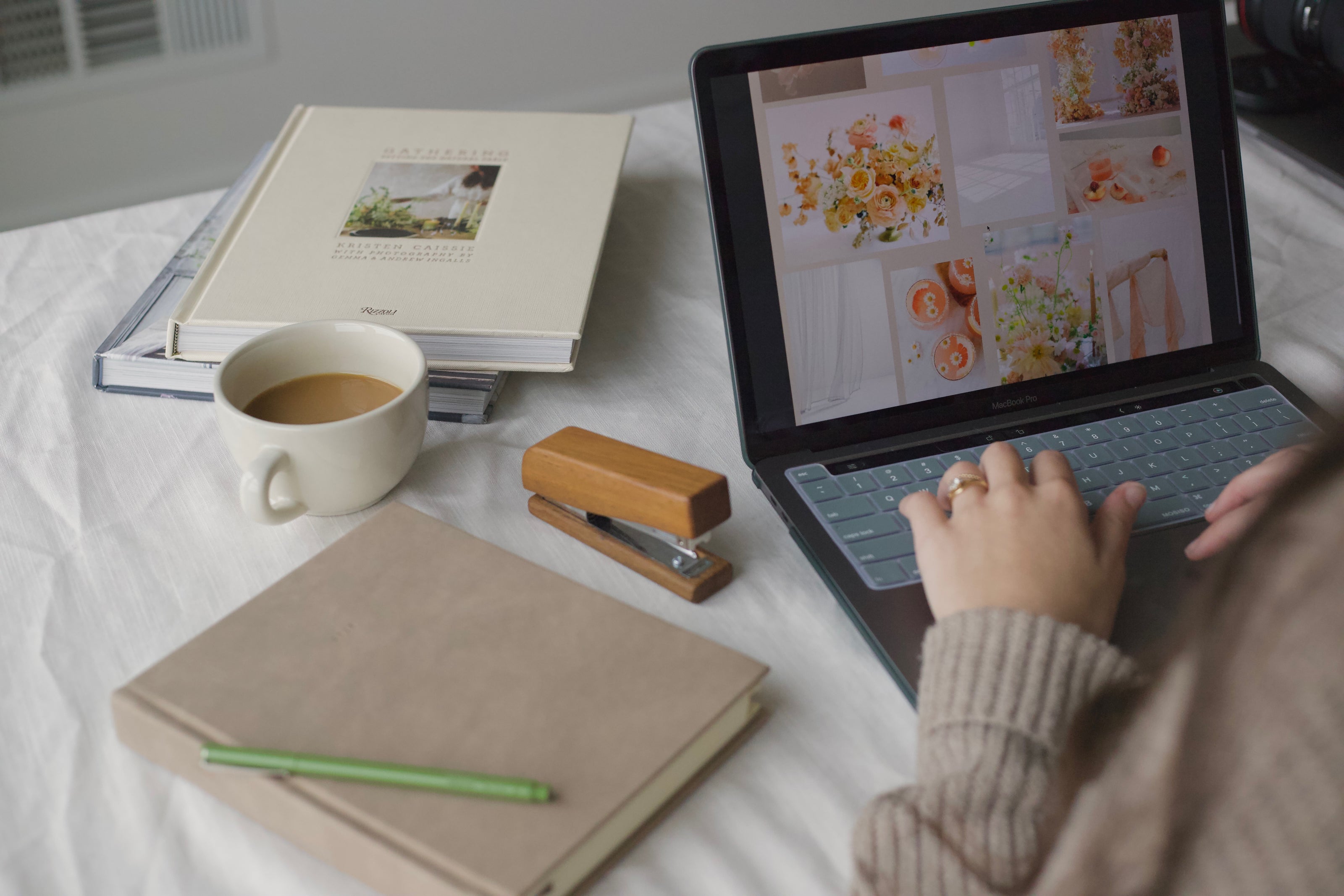 Person creating a flower quote on a laptop with books, coffee, and stationery items.