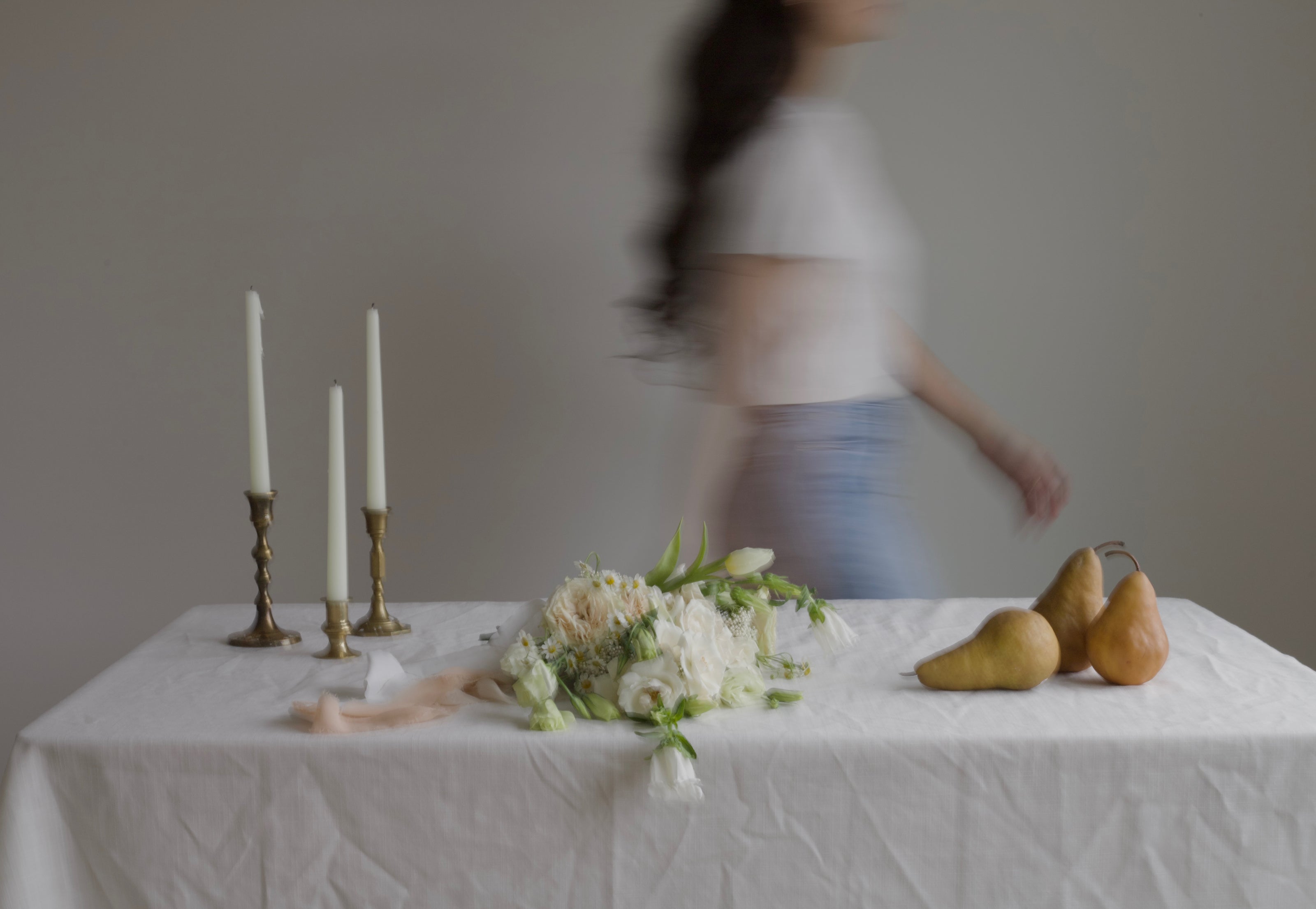 Table setting with candles, flowers, and pears, blurred person in the background