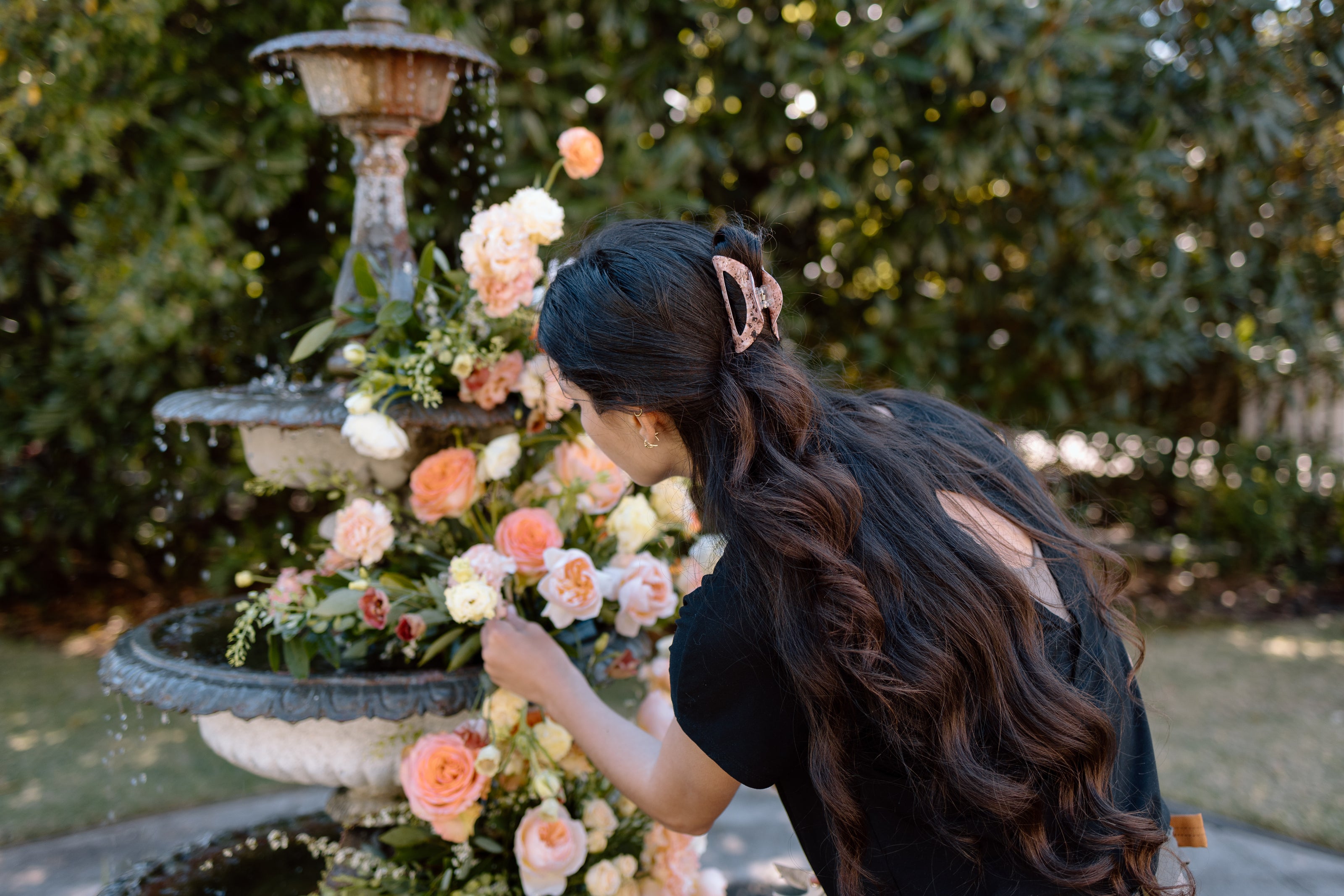Amber Payton arranging flowers in front of a fountain with greenery in the background