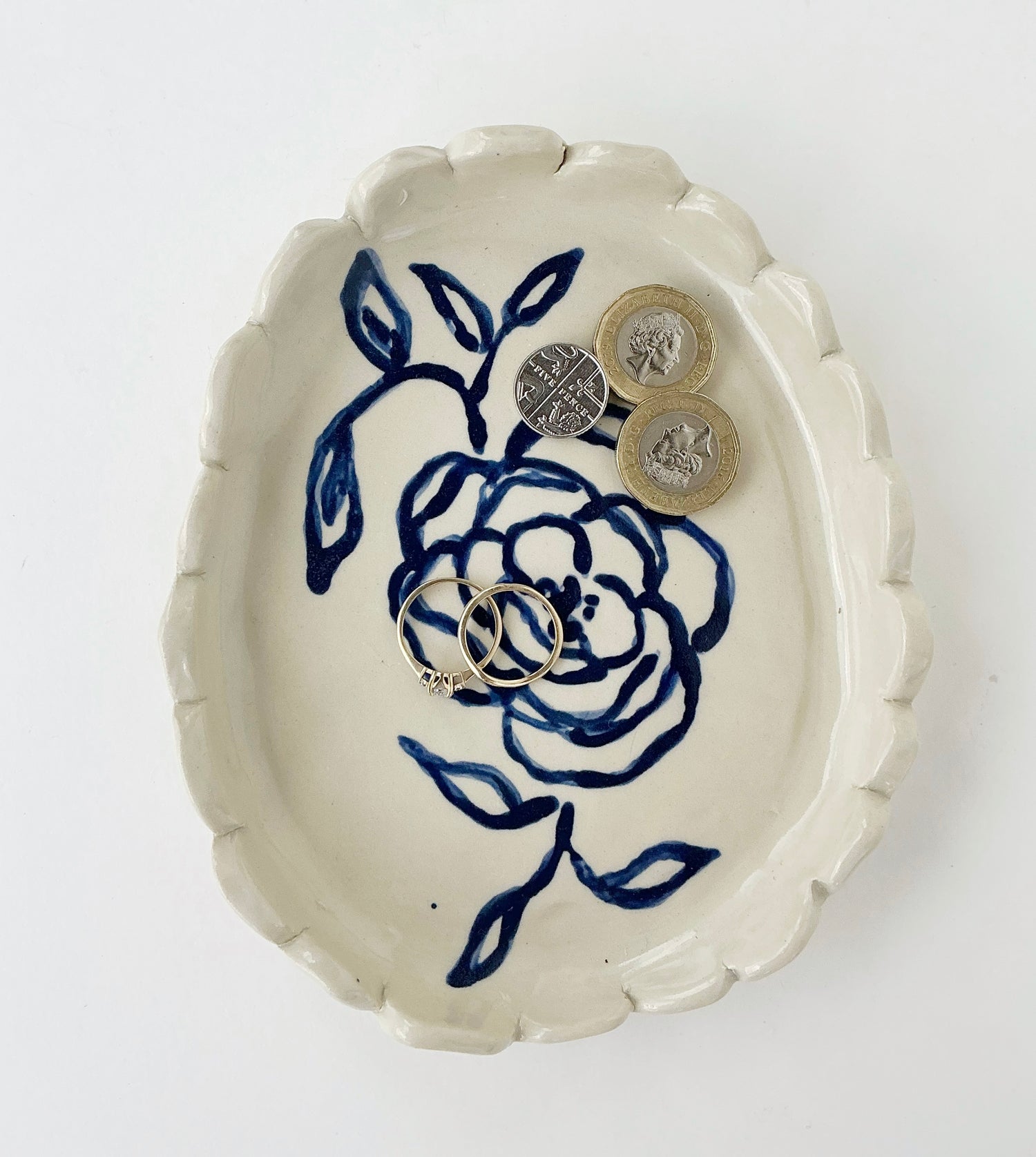 A ceramic trinket tray with a floral pattern in blue and white, displaying coins and jewelry on its surface.