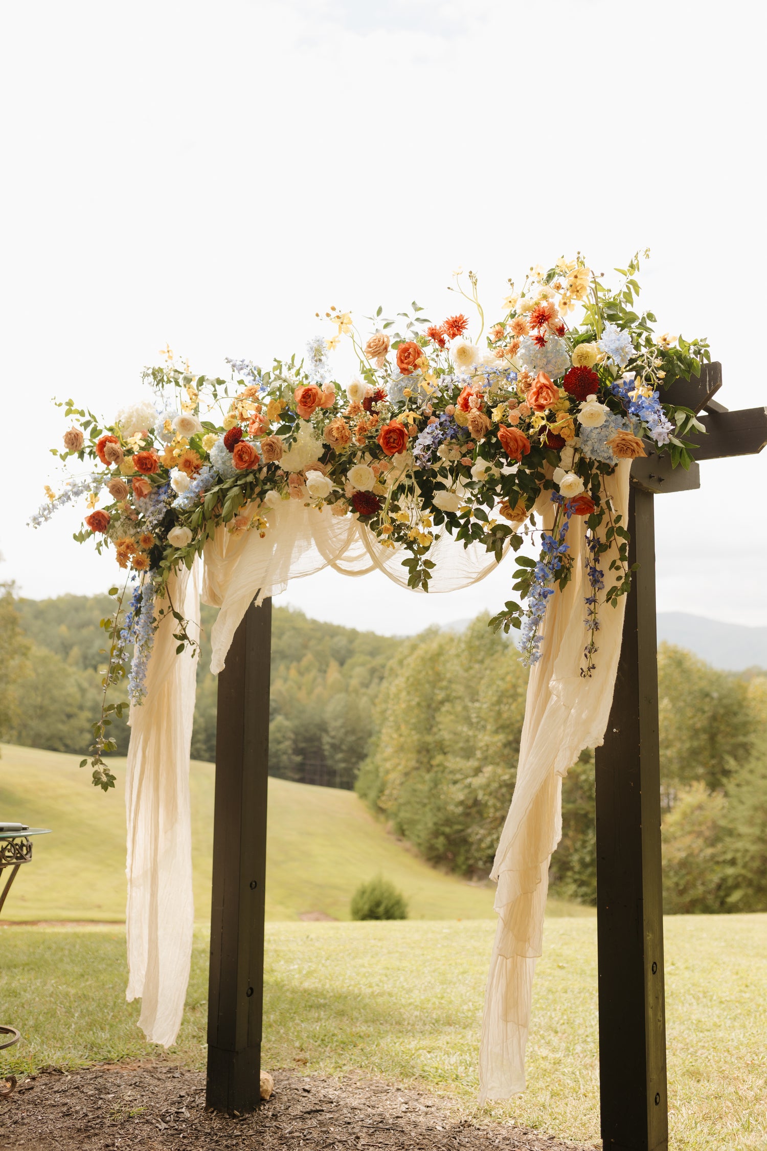 lush floral design wedding arch, arbor in shades of blue, rust, peach, ivory, yellow, with trailing greenery and trailing fabric. romantic arch atlanta georgia